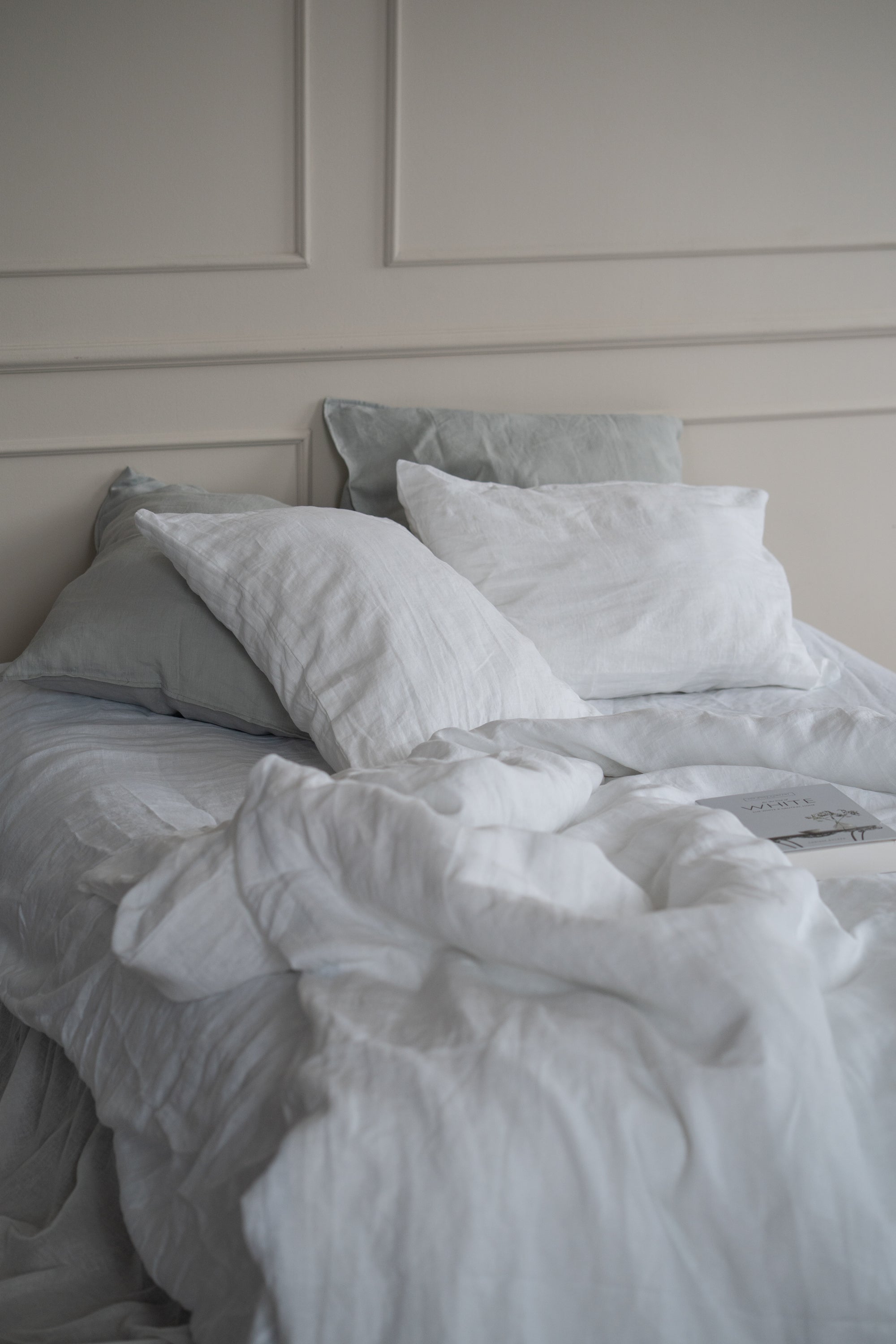 Neatly made bed with light gray bedding against a neutral wall.